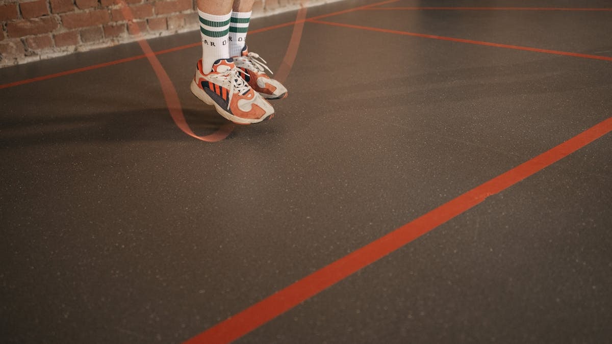 Feet of a person in sneakers skipping rope on an indoor gym floor.