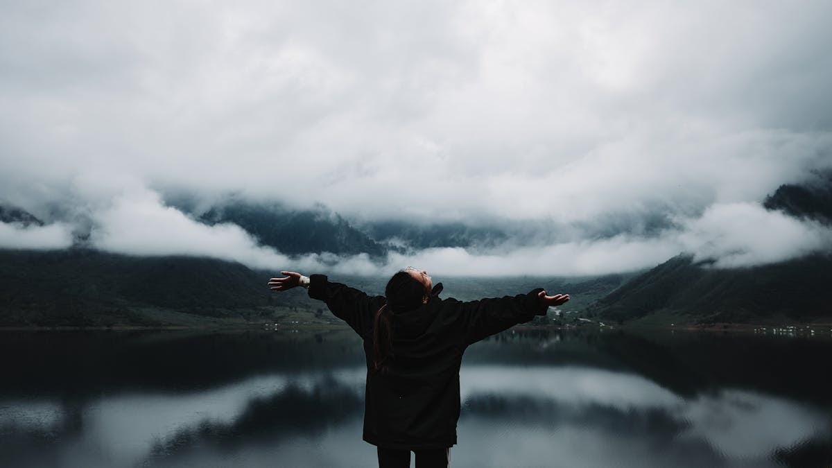 A person enjoys a sense of freedom by a misty mountain lake, embracing nature's tranquility.